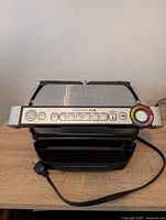 Closed Tfal OptiGrill unit showing front control panel with preset buttons and cooking progress dial.