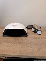 White UV nail lamp with opening and three gel polish bottles on wooden table