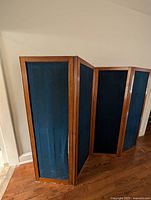 Front view of the vintage room divider showing the four oak frame panels with dark blue cloth coverings. Slight fabric damage is visible.