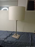 White IKEA table lamp with textured white lampshade and metal base on a blue cloth surface.