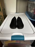 Pair of black slip-on Skechers shoes placed on a white plastic container lid, showing overall shape and condition.
