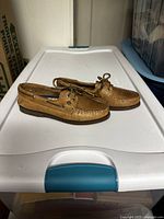 Full side view of the pair of tan women's Sperry boat shoes, showing leather upper, moc toe stitching, laces and rubber outsole.