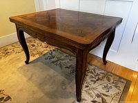 Front and side view of table showing marquetry top, carved apron, cabriole legs.