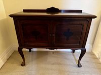 Front view of antique mahogany sideboard. Shows two paneled doors with ornate dark inlay and carved feet with claw detail.