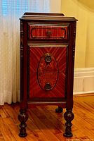 Front view of antique walnut end table showing mahogany veneer top and burled wood drawer fronts with decorative circular pulls and turned legs.