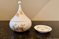 Candy dish with pointed lid and small plate featuring gold floral design on white porcelain, shown closed and open to display interior.