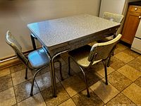 Full view of the vintage dining table with three matching chairs in a kitchen setting, showing the overall condition and design.
