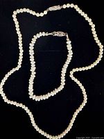 Freshwater pearl necklace and matching bracelet laid out on a black surface, showing both pearl strands and silver clasps.