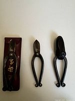 Top view of three pairs of Hasami floral scissors, one with brown leather case with Japanese gold script.