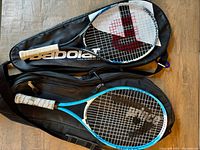 Two tennis rackets lying on top of the carry bags, showing both rackets with wrapped grips and racket heads with strings.