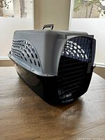 Closed view of the pet carrier showing black bottom, gray top, ventilation holes on the sides, and front metal door.