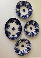 Three Claremont Flow Blue embossed bowls with deep blue floral patterns on white porcelain, arranged around blue and white Knox pattern serving dish.