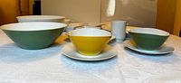 Front view of three serving bowls in green and yellow color exterior and white interior on white tablecloth