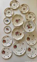 All porcelain plates and pedestal dishes arranged on surface showing floral designs and varied sizes.