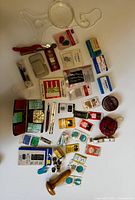 Overview photo of assorted sewing and crafting supplies organized on a white surface, including needles, threaders, pins, measuring tools, seam rippers, and various accessories.