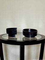 Two Ikebana containers shown side by side on a glass-top table. One is a semi-circular shape, the other is oval.