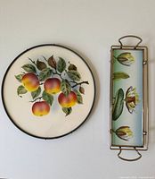 Pair of vintage serving dishes displayed from above, showing apple motif round plate and floral Art Nouveau rectangular tray.