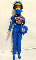 Front view of Barbie wearing racing suit and helmet, holding cap