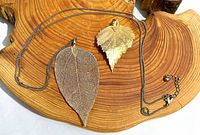 Long gold-tone leaf necklace and separate smaller pendant displayed on wood surface