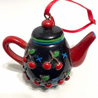 Side view of miniature teapot ornament showing cherry design, red handle, spout, and hanging ribbon