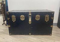 Front view of navy wooden steamer trunk with brass latches and central lock plate, showing surface wear and patina.