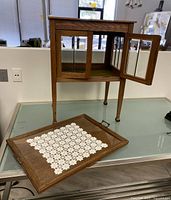 Wood cabinet with removable tray placed in front, tray top featuring glass insert and metal handles