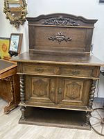 Front view of antique wooden sideboard showing carvings, drawer handles, cabinet doors, and leg detailing.