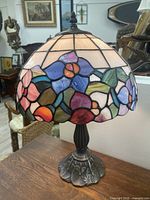 Full view of the lamp showing stained glass shade with floral motifs and metal base, highlighting colors and design.