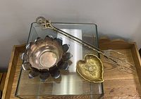 Photo showing three decorative bowls with petal edges and a pair of ornate brass tongs on a glass table.