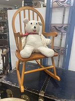 Children's wooden rocking chair with natural finish and stuffed bear placed on the seat to show scale and usage.