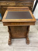 Front view of desk with hinged top closed, showing leather writing surface and carved columns