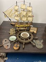 Full view of the nautical ensemble including the HMS Victory model ship, ship wheel barometer, decorative plate, brass anchor door knocker, framed maritime print, and vintage nautical items arranged on a dark wooden surface.