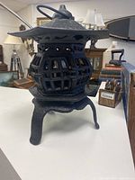 Black oriental style cast iron decorative lamp with a hexagonal body and latticework sides, standing on three legs. The hinged door is opened in some images to show the bulb inside.