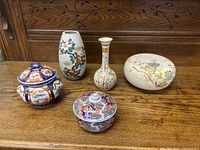 Five Oriental style ceramics including vases and lidded jars showing multicolor floral and geometric patterns on porcelain and ceramic material, arranged on wooden surface.