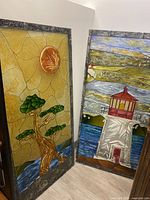 Two vertical painted glass panels with detailed nature-themed stained glass style art. Left panel shows Arbutus tree under an orange sun. Right panel shows a white lighthouse with red accents against water and hills.