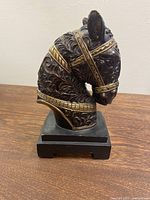 Front and side angled views of the brown resin horse bust sculpture with detailed carvings and gold decorative accents on the harness. Mounted on a black rectangular base.