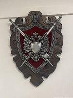 Full view of the decorative wall plaque showing wooden base and metal crest with crown and crossed swords on red background