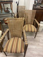 Set of three rustic wicker armchairs arranged together showing high woven backrests and padded striped fabric seats.