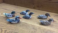 Six handcrafted wooden duck figurines, each painted differently, arranged on a wooden surface to show detail.