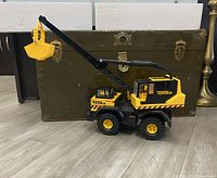 Side view of the Tonka toy crane truck showing the extendable arm raised with bucket attached, placed on floor beside a trunk.