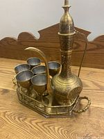 Front view of the vintage brass tea set showing teapot, serving tray and six cups arranged inside the tray on a wooden surface
