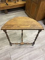 Front view of demi-lune table showing half-moon wooden top and three straight turned legs connected by stretcher base