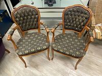Pair of vintage armchairs seen from the front, showing multicolor fabric upholstery, tufted backs, wooden frames with curved arms and legs.