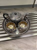 Vintage silver-plated tea set with teapot, creamer, sugar bowl, and tray arranged on a flat surface showing tarnished finish and antique detailing.