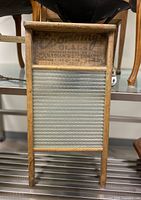 Front view of vintage washboard showing wooden frame and textured glass scrubbing surface with branding on the top panel.