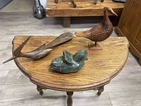 Three bird sculptures on a wooden table: two wood carved birds and one green marble bird sculpture, showing front view and detailing.
