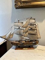 Front angle side view showing detailed sails, rigging, and wooden hull on base with nameplate.