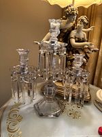 Front angle photo of the clear crystal antique Italian candelabra showing the three candle holders and hanging rectangular crystal prisms with a decorative figure in the background.