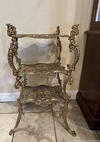 Front view of cast brass three-tier stand showing overall structure and decorative motifs