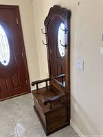 Side view of the antique wood hall tree showing storage bench with armrests and mirror reflecting front door.